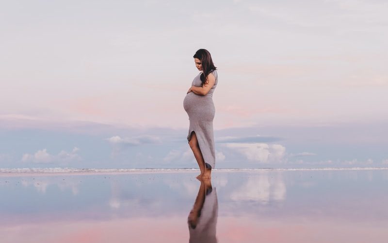 pregnant woman standing on calm body of water