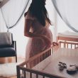 woman in white lace sleeveless dress standing beside brown wooden crib